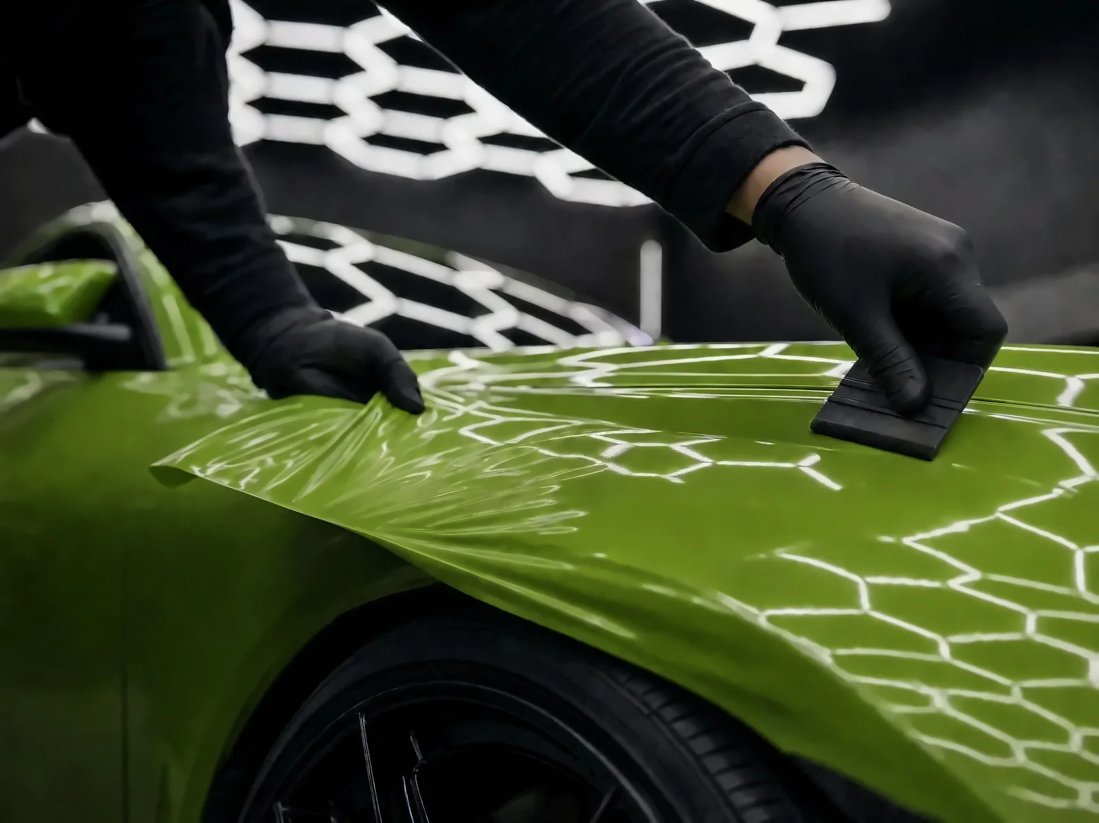 Installer's gloved hands stretching gloss green wrap film over a fender (studio illustration)